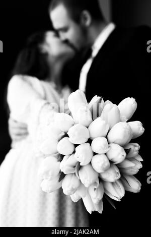 Bissing giovane coppia con un bouquet di fiori di tulipani bianchi in bianco e nero immagine, fuoco selettivo. Foto verticale. Foto Stock