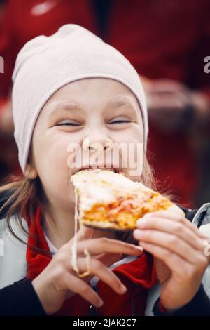 Una ragazza in un cappello con un pezzo di pizza. Una festa in casa nel cortile. Foto verticale. Foto Stock