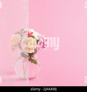 Bouquet di fiori in vaso di vetro nascosto dietro una tenda bianca su sfondo rosa. Concetto estivo minimo. Isometrico astratto. Quadrato con copia Foto Stock