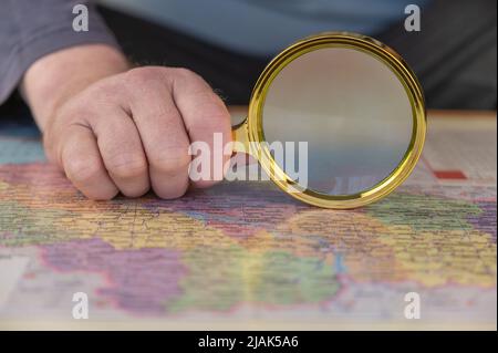 Un uomo tiene una lente d'ingrandimento in mano sopra una mappa. Uomo di mezza età con una lente d'ingrandimento in una cornice d'oro. I nomi sono scritti in ucraino. Foto Stock