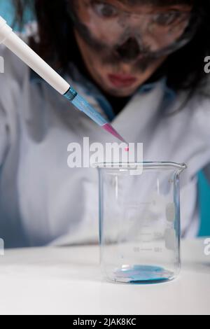 Primo piano di scienziato stolto pazzo con pipetta facendo esperimenti mentre si siede alla scrivania. Wacky insane chemist utilizzando contagocce per miscelare composti chimici sperimentali dopo l'esplosione in laboratorio. Foto Stock