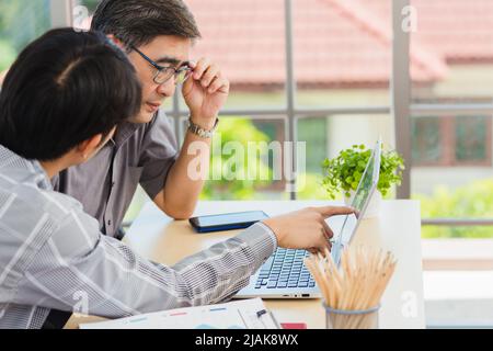 Giovane uomo asiatico che insegna padre senior come utilizzare un moderno computer portatile insieme nel soggiorno di casa, Son aiutare papà a utilizzare il portatile per Foto Stock
