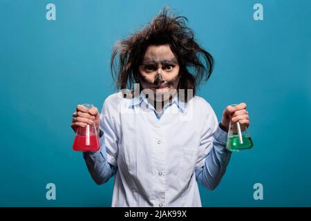 Chemist insano e arrabbiato con faccia sporca e capelli sudicie che tengono vasi di vetro riempiti di composti chimici tossici. MAD e lo scienziato arrabbiato con l'aspetto stravagante infuriato dall'esperimento fallito. Foto studio Foto Stock