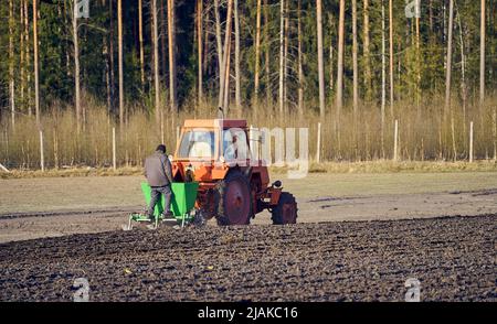 Il trattore aratura il campo, coltiva il terreno per la semina del grano. Agricoltore in piedi dietro il trattore durante il processo. Il concetto di agricoltura e macchine agricole. Foto Stock