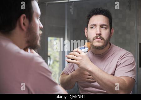 Riflesso della rasatura del giovane uomo con il rifinitore davanti allo specchio. Foto Stock