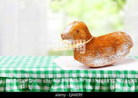 Modello carta di Pasqua. Una tradizionale torta di agnello pasquale su un piatto bianco su una tovaglia verde controllata contro uno sfondo sfocato finestra. Spazio per des Foto Stock