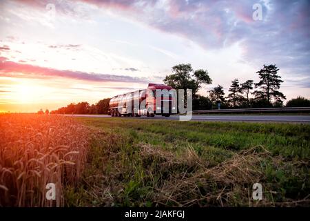 Un moderno camion con una petroliera semi-rimorchio trasporta merci pericolose sullo sfondo di un tramonto in estate. Trasporto di carichi liquidi Foto Stock