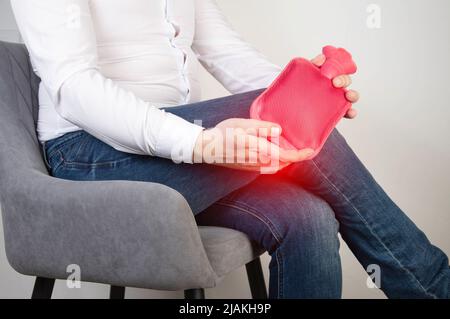 Un lavoratore di ufficio maschio tiene un cuscinetto di riscaldamento con acqua calda vicino all'articolazione del ginocchio. Trattamento del dolore al ginocchio con terapia termica, artrite reumatoide Foto Stock