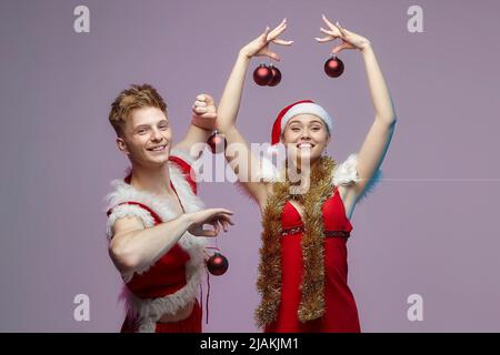 Ragazzo e ragazza in costumi di Santa a una foto sparare in Studio. Guy mette le decorazioni di Natale su una ragazza Foto Stock