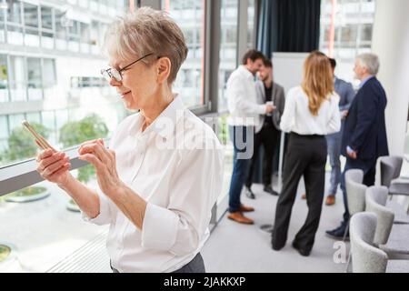 La donna in ufficio scrive un messaggio di testo sullo smartphone con il team in background Foto Stock