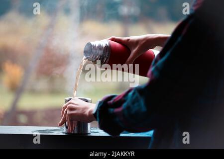 Una ragazza versa il tè da un thermos su uno sfondo di montagne Foto Stock