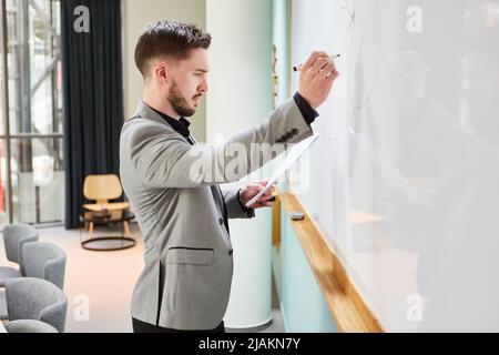 Giovane uomo come scienziato o oratore che fa una presentazione sulla lavagna Foto Stock