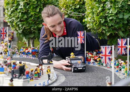 Model Maker Freya Groom colloca una replica della Regina Elisabetta II, riimmaginata in mattoni LEGO, in un veicolo animato come parte del Platinum Jubilee Display presentato oggi al LEGOLAND Windsor Resort. La regina animata e il veicolo ha preso 15hrs per costruire utilizzando 1.350 mattoni. LEGOLAND Windsor Resort ha presentato oggi i suoi modelli di ispirazione regale per celebrare il Giubileo del platino della Regina. Il numero complessivo di mattoni utilizzati è stato di 18.001 e i modelli hanno impiegato un totale di 281,5 ore per finire. Il display include anche una festa di strada e scena pic-nic, così come le versioni in miniatura dei reali, l'albero di Foto Stock