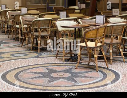 Posti a sedere e tavoli all'aperto presso un French Cafe nel centro di Parigi. Tavoli e sedie con un bel pavimento a mosaico. Nessuna gente Foto Stock