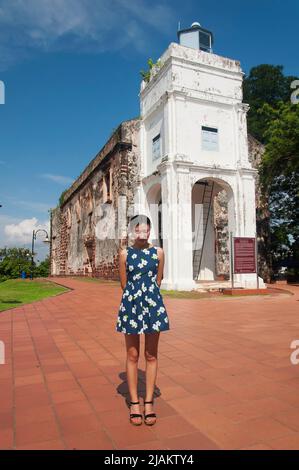 Una donna cinese che si erge di fronte alle rovine storiche della Chiesa cattolica di San Paolo e al faro di Melaka in Malesia in una giornata di cielo blu e soleggiato. Foto Stock