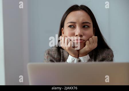 Sconvolto donna d'affari asiatica che lavora su un notebook in ufficio e guarda via Foto Stock