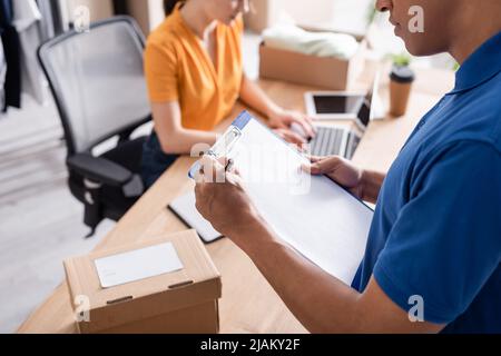 Vista ritagliata del corriere africano americano che scrive sugli appunti nel negozio in linea di fotoricettore Foto Stock