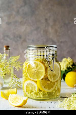 Acqua o sciroppo di sambuco fatti con fiori freschi e limoni come ingredienti di base. Sfondo grigio Foto Stock