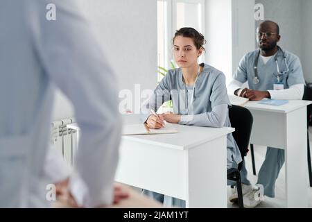 Studenti di medicina in seduta uniforme su scrivanie imparando come fornire il primo soccorso durante la formazione Foto Stock