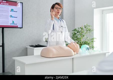 Medico femminile maturo che parla delle regole del primo soccorso utilizzando manichino durante la formazione medica Foto Stock