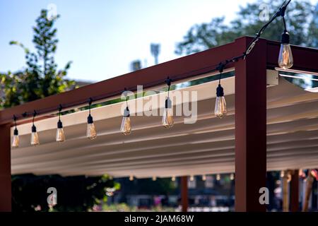 tenda tessile nel giardino gazebo telaio in legno con una ghirlanda di corde di retro edison lampadine di lampade di illuminazione incandescente con luce calda acceso Foto Stock