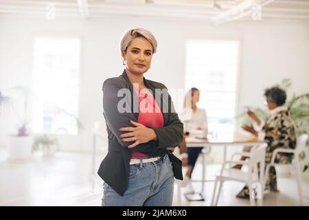 Giovane donna d'affari che guarda la macchina fotografica mentre si trova in una moderna sala riunioni. Giovane donna d'affari fiduciosa che partecipa a un incontro con il suo team Foto Stock