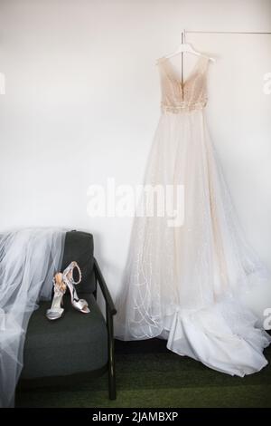 Abito da sposa appeso alla parete e scarpa sulla sedia Foto Stock