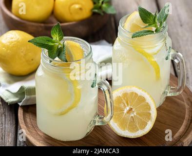 Due bicchieri di limonata con menta e limone su un vassoio di legno con ciotola di limoni sullo sfondo Foto Stock