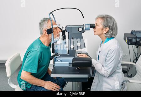 Esame visivo e diagnostica visiva. Optometristo femminile che fa il test della vista per l'uomo anziano alla clinica moderna di oftalmologia Foto Stock