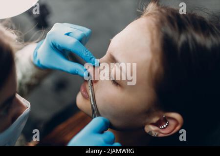 Giovane donna che fa piercing naso anello al salone di bellezza studio Foto Stock