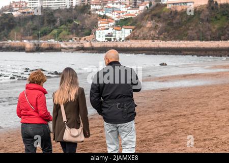 Famiglia composta da madre, padre e figlia adolescente che cammina lungo la spiaggia in una nuvolosa giornata invernale Foto Stock