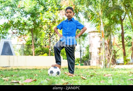 Il bambino campione sta in piedi con sicurezza sul calcio guardando la macchina fotografica al parco - concetto di competizione, attività sportiva e determinazione Foto Stock