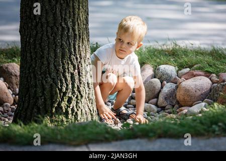 Un bambino gioca con i ciottoli nel parco cittadino. Il concetto di ricreazione, gioco e lo sviluppo delle abilità motorie dei bambini. Foto di alta qualità. Foto Stock