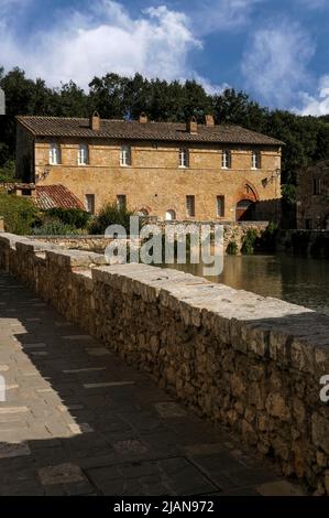 Edifici in pietra toscane color miele circondano il bagno di Santa Caterina del 16th secolo, una piscina rettangolare nel centro di bagno Vignoni, Toscana, Italia, che contiene acqua calda di sorgente vulcanica che sgorga dal profondo sotterraneo. Le proprietà calmanti e curative dell'acqua fumante sono state godute da Etruschi, Romani, Santa Caterina da Siena, il governatore mediceo Lorenzo il magnifico, Papa Pio II, lo scrittore Charles Dickens e il Marchese de Sade. Foto Stock