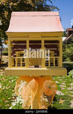 Cassetta postale in legno a 1800s chiodati in miniatura con veranda gialla e tetto in lamiera arancione nel cortile anteriore in autunno. Foto Stock