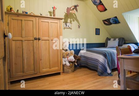 Peluche giocattoli in cestino di vimini e armoire in camera da letto al piano superiore all'interno del vecchio casolare di Canadiana 1832 stile fieldstone casa. Foto Stock