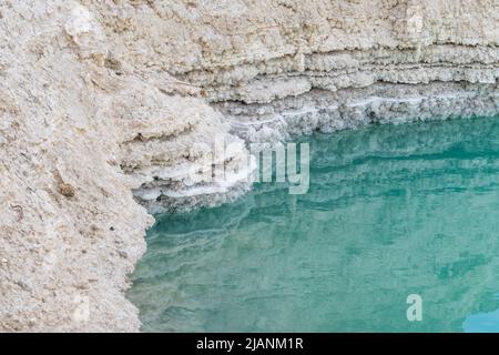 Buca piena di acque turchesi, vicino alla costa del Mar Morto. Leyers di fango e sale. Foro formato quando il sale sotterraneo è dissolto da intrusione di acqua dolce, dovuto la caduta continua del livello del mare. Foto Stock