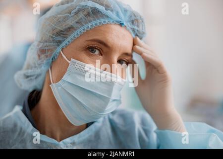 Primo piano di un chirurgo stanco in maschera in piedi in sala operatoria dopo un intervento chirurgico importante Foto Stock