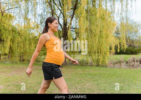 Donna incinta che cammina fuori nel parco cittadino durante l'estate per un sano allenamento del corpo. Passeggiata cardio durante la gravidanza Foto Stock