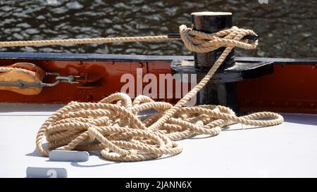 Un mucchio di corda sul ponte di una nave. È legato a un bullard. È collegato con una puleggia di legno. Foto Stock