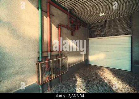 Ampio angolo di vista di un ingresso a un garage di un moderno edificio di appartamenti con un cancello bianco chiuso e tre tubi a gas (rosso e verde) in ingresso Foto Stock