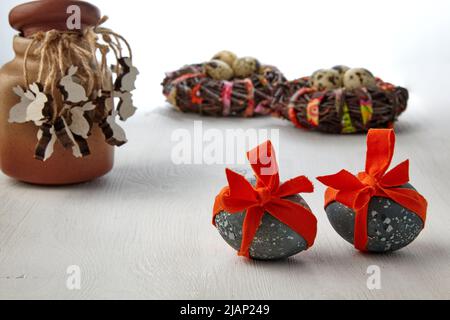 Uova di pollo dipinte legate con un nastro rosso e figurine di lepri di legno sullo sfondo dei nidi di uccello su uno sfondo bianco. Carta di Pasqua Foto Stock