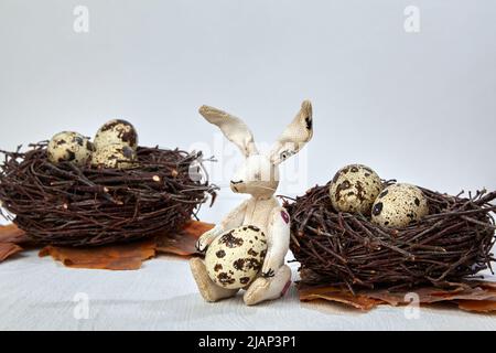 Peluche giocattolo e uova di quaglia nei nidi su uno sfondo bianco di legno. Concetto di Pasqua Foto Stock