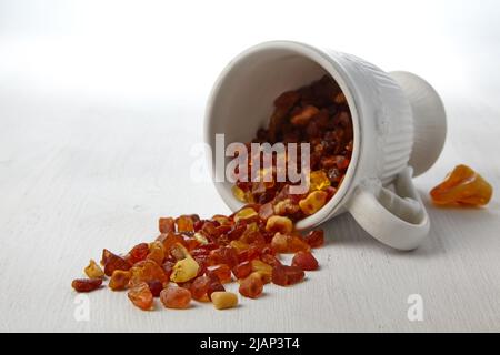 Ambra crudo in una tazza di ceramica cosparso su un tavolo di legno bianco. Foto Stock