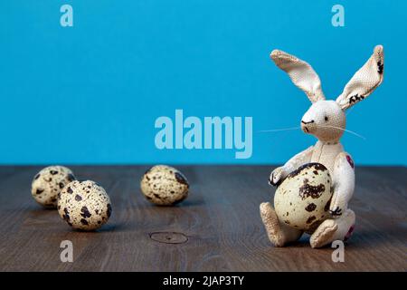 Soffice lepre giocattolo e quaglia uova macchiate su uno sfondo di legno marrone e blu. Banner di Pasqua Foto Stock