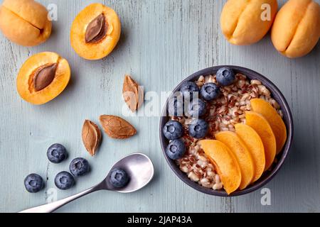 Colazione vegetariana. Fiocchi d'avena a grani interi con fette di albicocca e mirtilli su un tavolo in legno dipinto Foto Stock