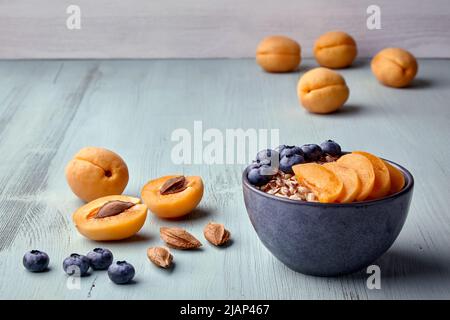 Colazione energetica. Fiocchi d'avena a grani interi con fette di albicocca e mirtilli su un tavolo in legno dipinto Foto Stock