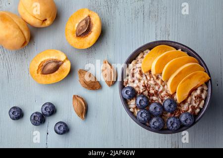 Fiocchi d'avena a grani interi con fette di albicocca e mirtilli su un tavolo in legno dipinto. Colazione vegana Foto Stock