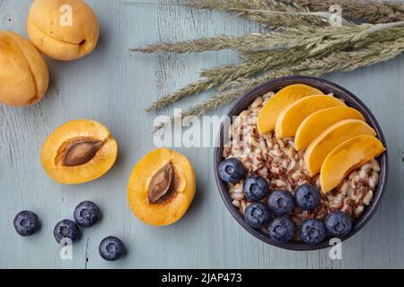 Fiocchi d'avena a grani interi con fette di albicocca e mirtilli su un tavolo in legno dipinto. Colazione vegana Foto Stock