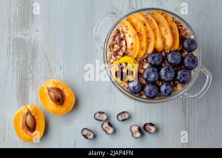 Fiocchi d'avena a grani interi con fette di albicocca e mirtilli su un tavolo in legno dipinto. Colazione vegetariana Foto Stock